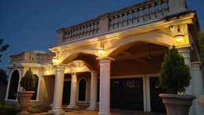 A grand building with a covered entrance, large columns, and a balcony with balustrades. - Villa San Juan a special place in Tela (El Triunfo de La Cruz)