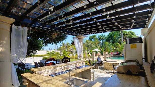 An outdoor bar area with a stone counter, seating, and a view of a pool and greenery. - Villa San Juan a special place in Tela (El Triunfo de La Cruz)