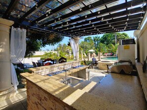 An outdoor bar area with a stone counter, seating, and a view of a pool and greenery. - Villa San Juan a special place in Tela (El Triunfo de La Cruz)