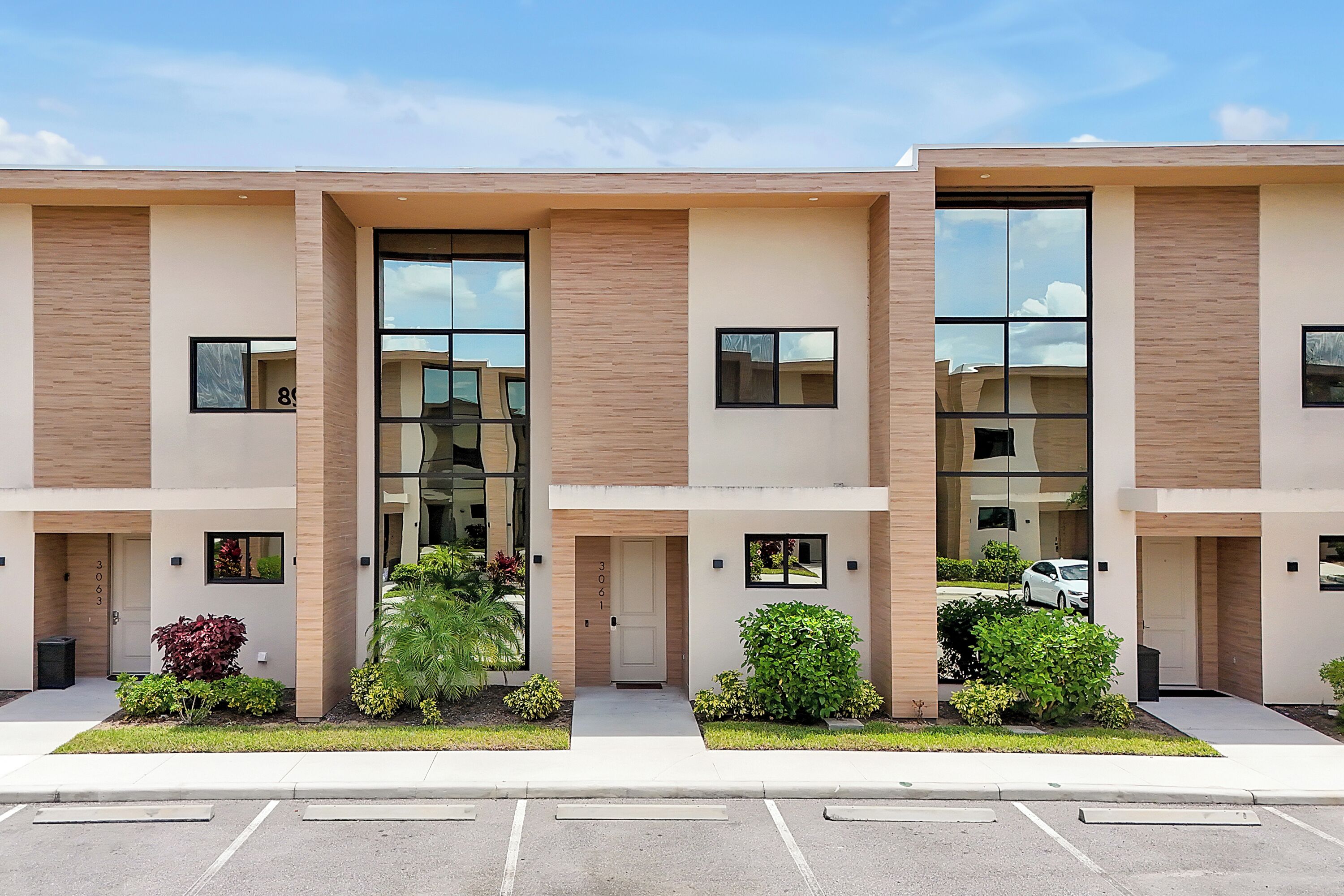 A modern multi-story building with a clean, minimalist design, featuring large windows and a parking lot in front.