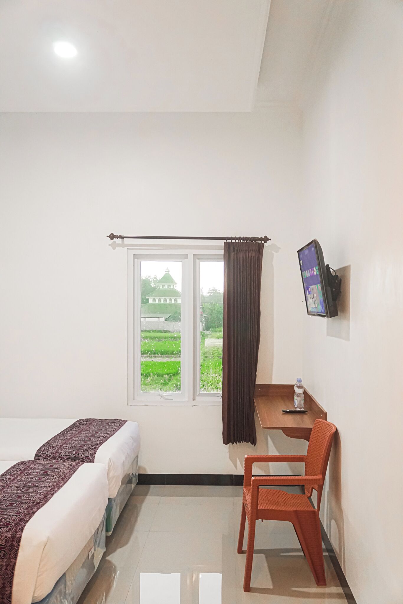 Habitación de hotel con cama, escritorio, silla, televisor y ventana con cortina.