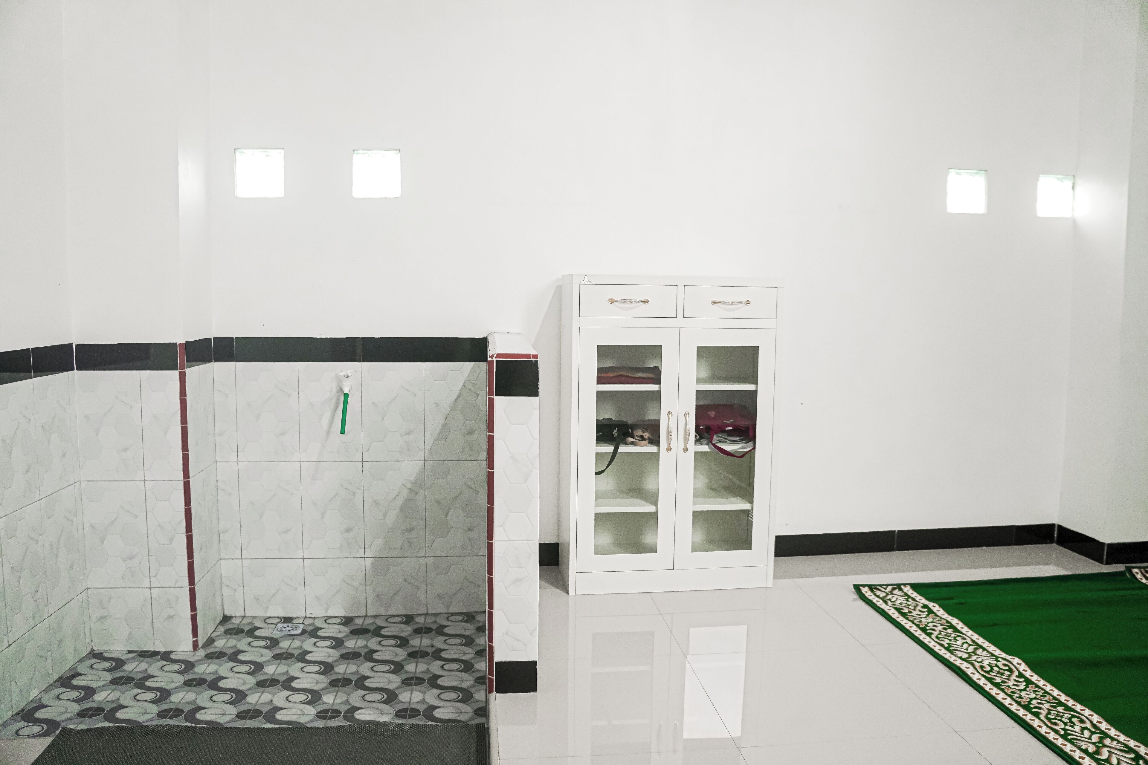 A room with a tiled floor, a cabinet with glass doors, and a green carpet.