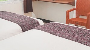 Ein Hotelzimmer mit zwei Betten, einem Fernseher, der 'Avengers' zeigt, einem Fenster mit Vorhang und einem Regal mit Wasserflaschen.