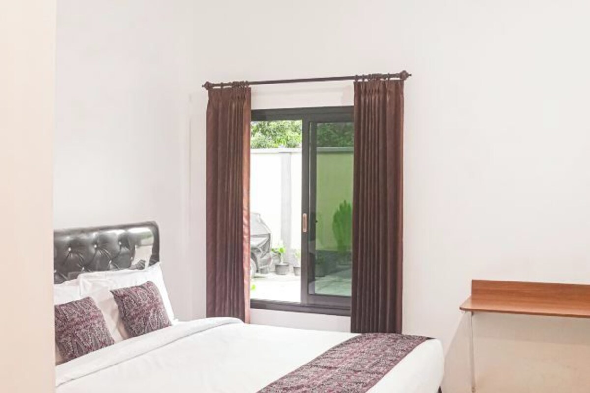 A bedroom with a bed, a wooden nightstand, and a sliding glass door leading to an outdoor area.