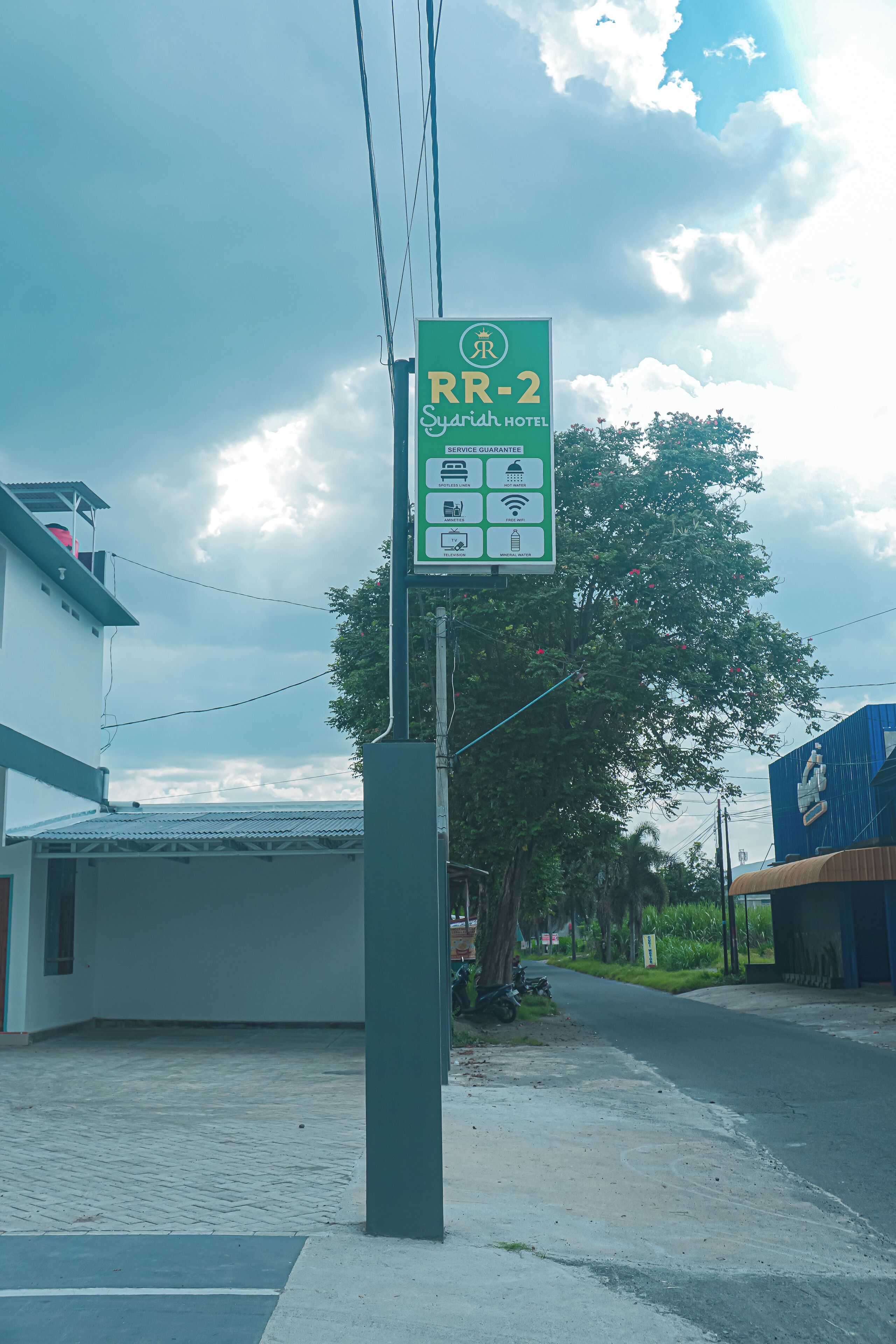 A sign for RR-2 Syariah Hotel with service guarantees and amenities icons.