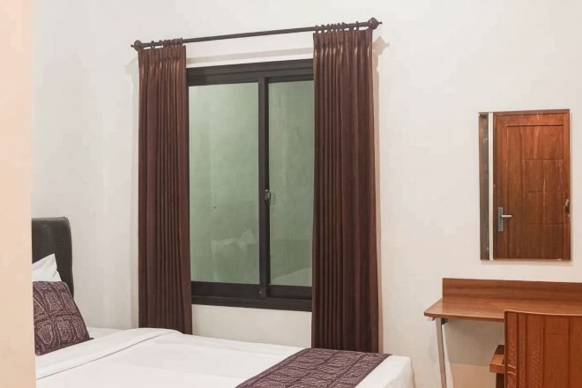 A bedroom with a bed, a window with curtains, a wooden door, and a small desk.
