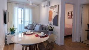 A modern living room with a round dining table, grey sofa, and a bed in the adjacent room. - Comfortable apartment for up to 3 people near USP - Shopping - Aeroclube (Jardim Brasil Bauru)