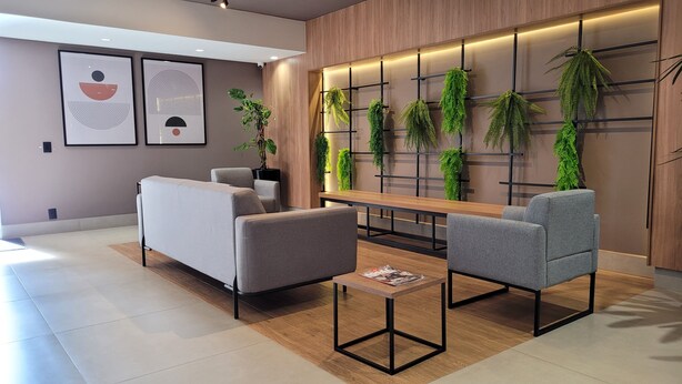 A modern waiting area with a sofa, two armchairs, a wooden table, and a wall-mounted plant display. - Comfortable apartment for up to 3 people near USP - Shopping - Aeroclube (Jardim Brasil Bauru)