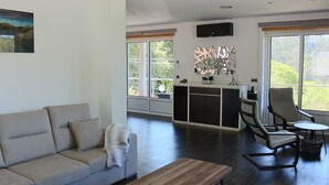 A spacious living room with a beige sofa, a wooden coffee table, and a seating area with two chairs and a small table. A large window provides a view of greenery outside. - EXCLUSIVE HOUSE WITH POOL IN GONDOMAR (gondomar)