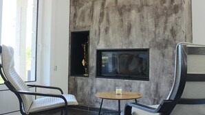 A modern living room with a large TV mounted on a textured wall, two lounge chairs, and a small round table with a glass of orange juice. - EXCLUSIVE HOUSE WITH POOL IN GONDOMAR (gondomar)