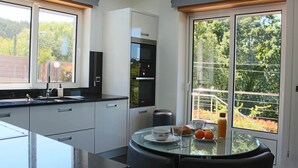 A modern kitchen with a large window, a glass table, and a view of trees. - EXCLUSIVE HOUSE WITH POOL IN GONDOMAR (gondomar)