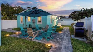 Un jardin avec une maison bleue, un espace salon extérieur et un barbecue.