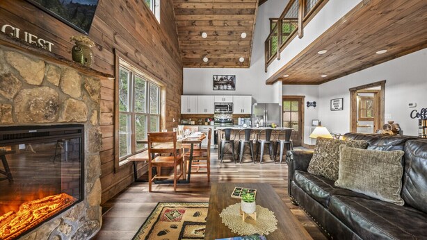 A cozy interior with a stone fireplace, wooden beams, a dining area, and a leather sofa.