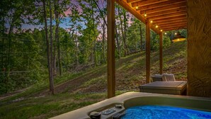 A hot tub with a wooden deck and a view of a forested hillside.