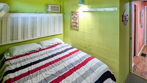 Una stanza con un letto, un ventilatore a soffitto, un condizionatore e una porta che dà su un'altra stanza.