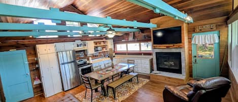 L’intérieur chaleureux d’un chalet avec un plafond en bois, un coin repas, une cheminée et une porte portant l’inscription « LAC ».