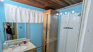 Un bagno con soffitto in legno, parete blu, lavabo bianco, specchio e cabina doccia in vetro.