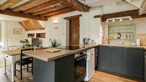 A kitchen with a central island, wooden beams, a refrigerator, and a sink.