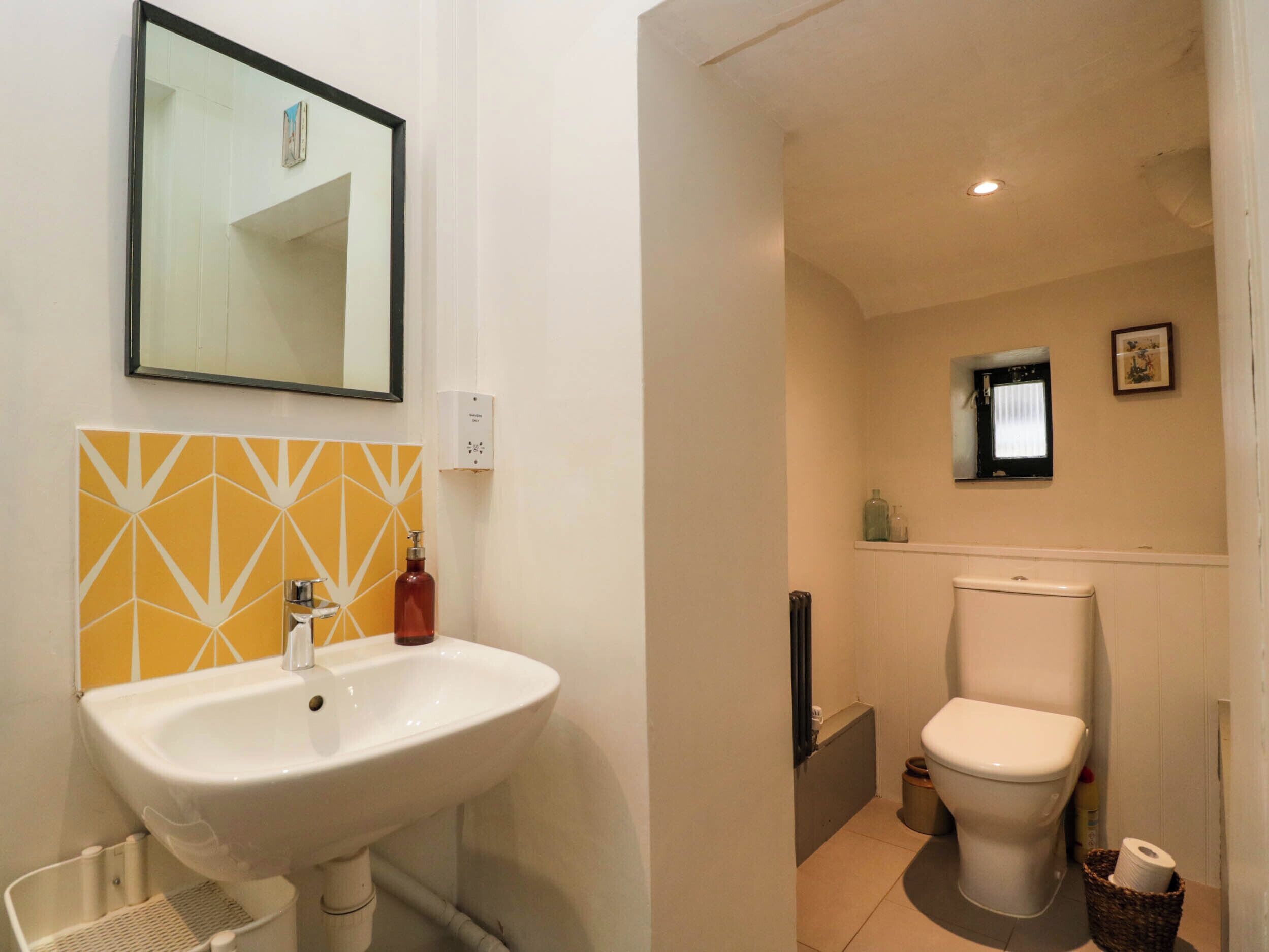 A bathroom with a white sink, a mirror, a toilet, and a small window.