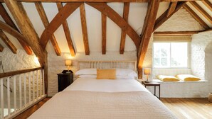 A bedroom with a large bed, wooden beams, white walls, and a window.