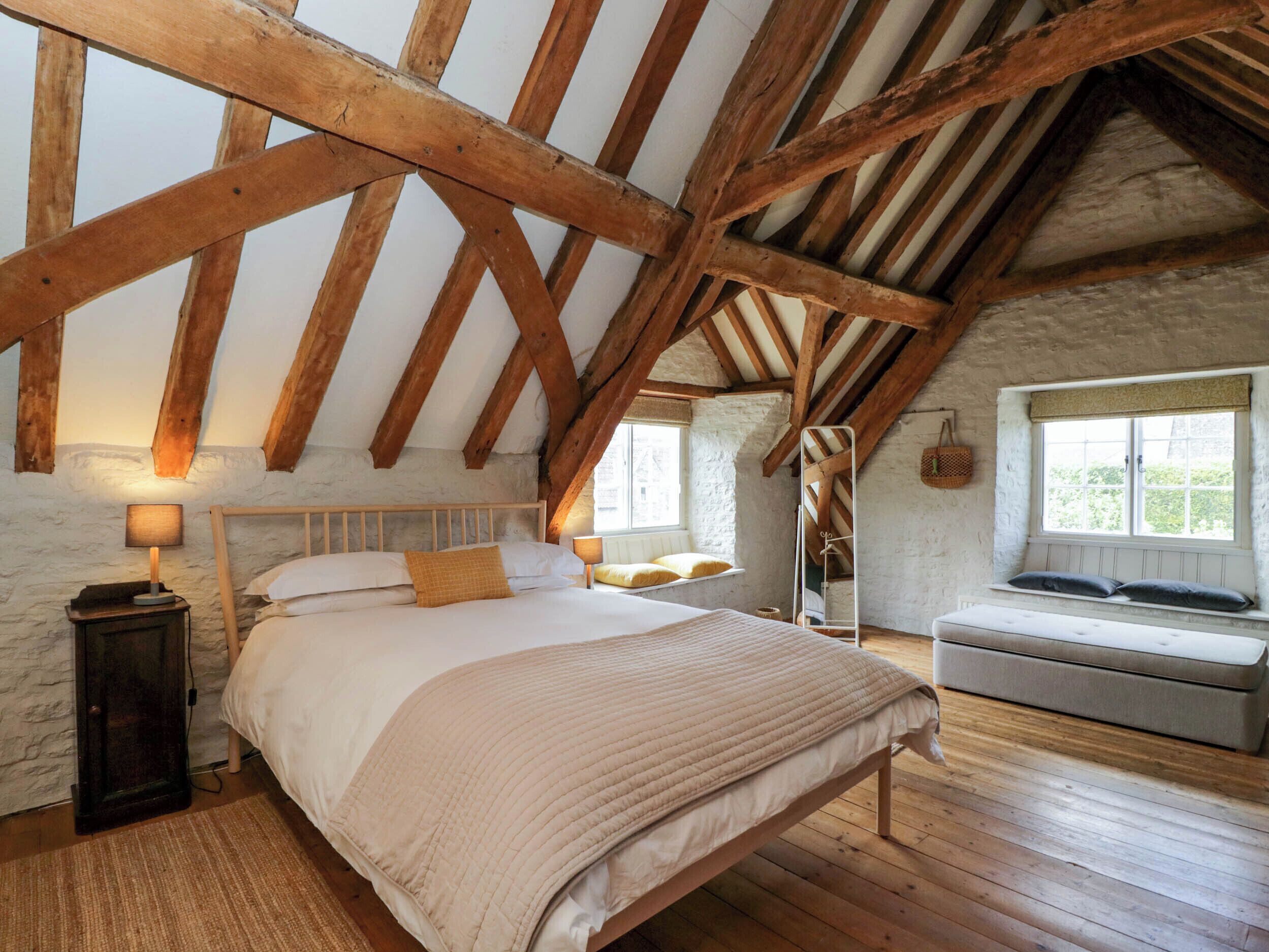 Une chambre avec un plafond en bois, un lit avec une literie blanche, une table de chevet avec une lampe et une fenêtre donnant sur un paysage verdoyant.