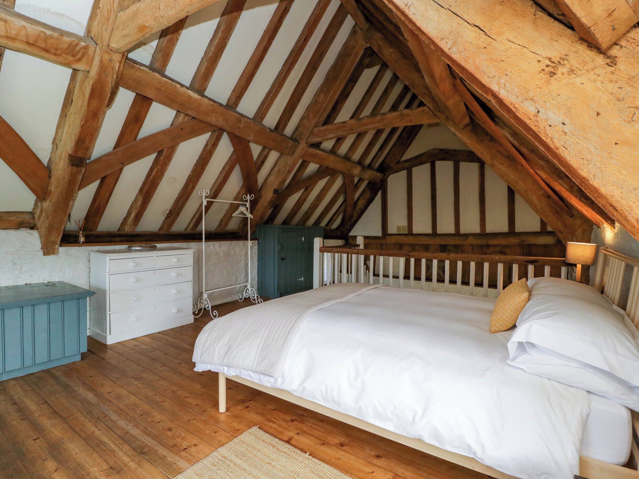 A bedroom with a sloped ceiling, wooden beams, a bed, a dresser, and a hanging rack.