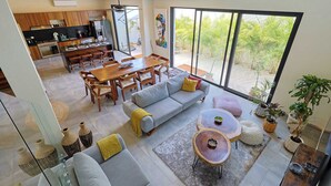 Amplia sala de estar con mesa de comedor, sofá y mesa de centro, conectada a una cocina y un balcón con plantas.