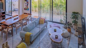 Amplia sala de estar con mesa de comedor, sofá y mesa de centro, ventanas grandes y lámpara colgante.