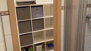 Un baño con zona de ducha, inodoro y un armario con varios estantes.