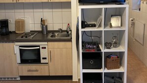 Una kitchenette compacta con microondas, pileta y una pequeña mesada. Un televisor de pantalla plana está montado en un estante blanco sobre la mesada.