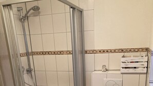 Un baño con ducha de vidrio, inodoro y un pequeño estante.