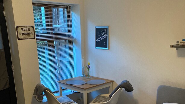 Un dormitorio con una cama, un escritorio y dos sillas, una ventana con persianas, y una puerta.