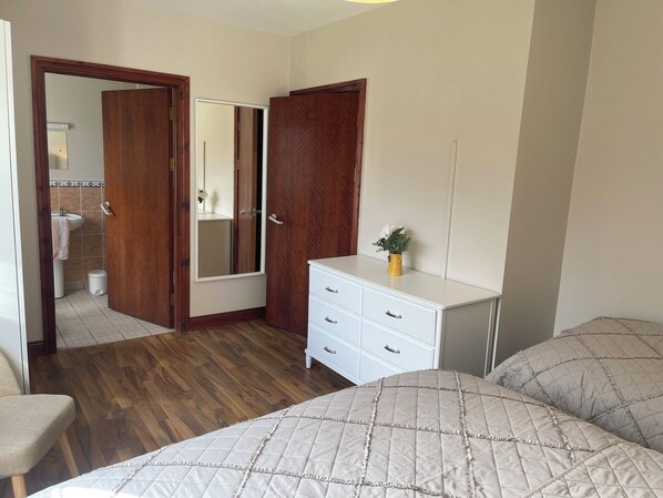A bedroom with a wooden floor, a white dresser, a bed with a quilted cover, and a mirror on the wall.
