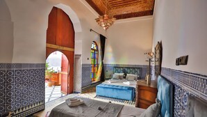 A room with a bed, a blue ottoman, a wooden door, and a stained glass window. - riad dar jeanne  (Fès)