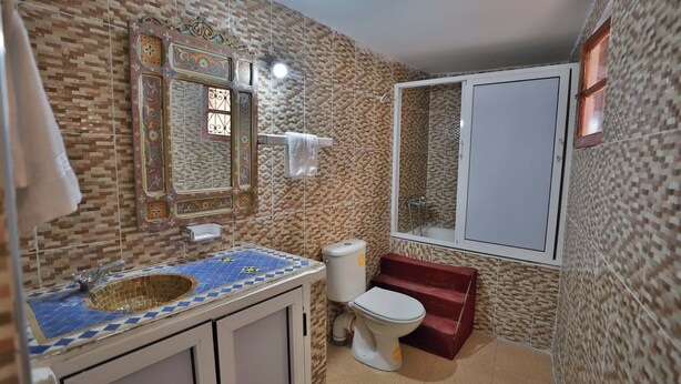 A bathroom with a patterned tile wall, a sink with a blue and yellow mosaic countertop, a white toilet, and a mirror with an ornate frame. - riad dar jeanne  (Fès)