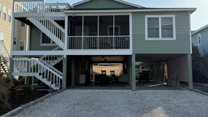 A two-story house with a covered garage, a front porch, and a staircase leading to the upper level. - Gorgeous Home on Sunset Beach, Just Steps from the Shore! (Sunset Beach)