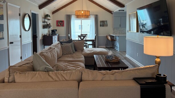 A cozy living room with a high ceiling, a large sofa, a dining area, and a TV mounted on the wall. - Gorgeous Home on Sunset Beach, Just Steps from the Shore! (Sunset Beach)