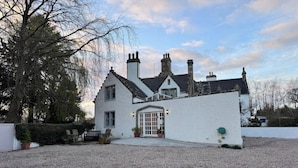 A white building with a symmetrical facade, multiple chimneys, and a gravel driveway.