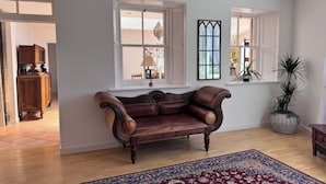 A room with a leather sofa, a patterned rug, and two windows with white frames.