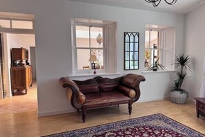 Una habitación con sofá de cuero, alfombra estampada y dos ventanas con marcos blancos.