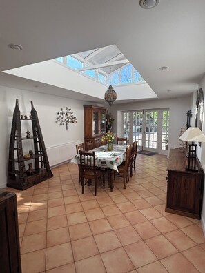 A dining area with a high ceiling and skylight, wooden furniture, and a tiled floor.