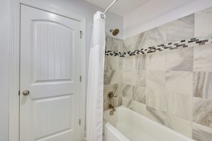 Ein Badezimmer mit weißer Tür, einer Duschvorhang und einer Badewanne mit Marmorfliesen.