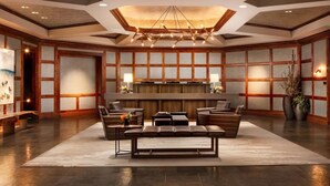 A spacious lobby with a central seating area, a modern chandelier, and a large wooden panel wall.