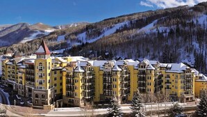 A multi-story hotel with a yellow facade, surrounded by snow-covered mountains and trees.