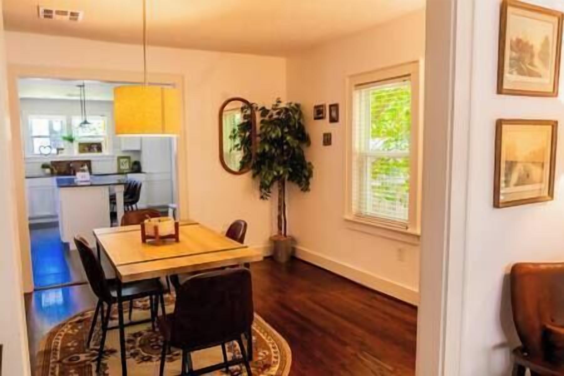 A dining area with a wooden table and chairs, a potted plant, and a window with a view of greenery.