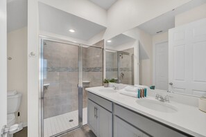 Une salle de bain moderne avec une douche à parois de verre, un grand miroir et un lavabo blanc avec un meuble-vasque.