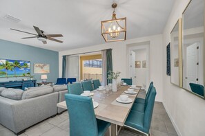 A dining area with a long table set for six, teal chairs, and a ceiling fan.