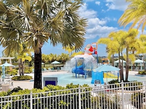 A water park with a water slide, palm trees, and lounge chairs.