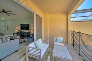 Un balcon avec des meubles blancs, un ventilateur de plafond et un téléviseur à l’arrière-plan.
