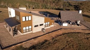 Un bâtiment moderne à deux étages, doté d’un toit plat, de grandes fenêtres et d’un espace extérieur couvert aménagé avec des sièges.